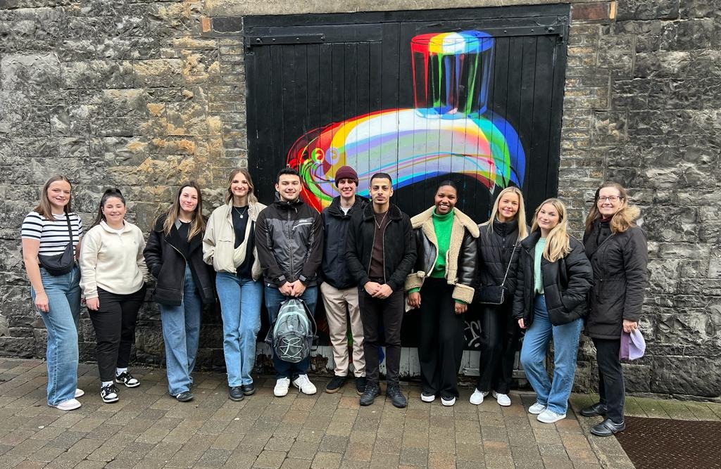 Group of students standing in front of gates painted with Guinness toucan in bright colours