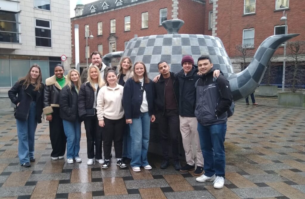 Group of students standing in front of large sculpture of a teapot